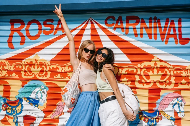 Two friends wearing sunglasses posing in front of a striped carnival mural